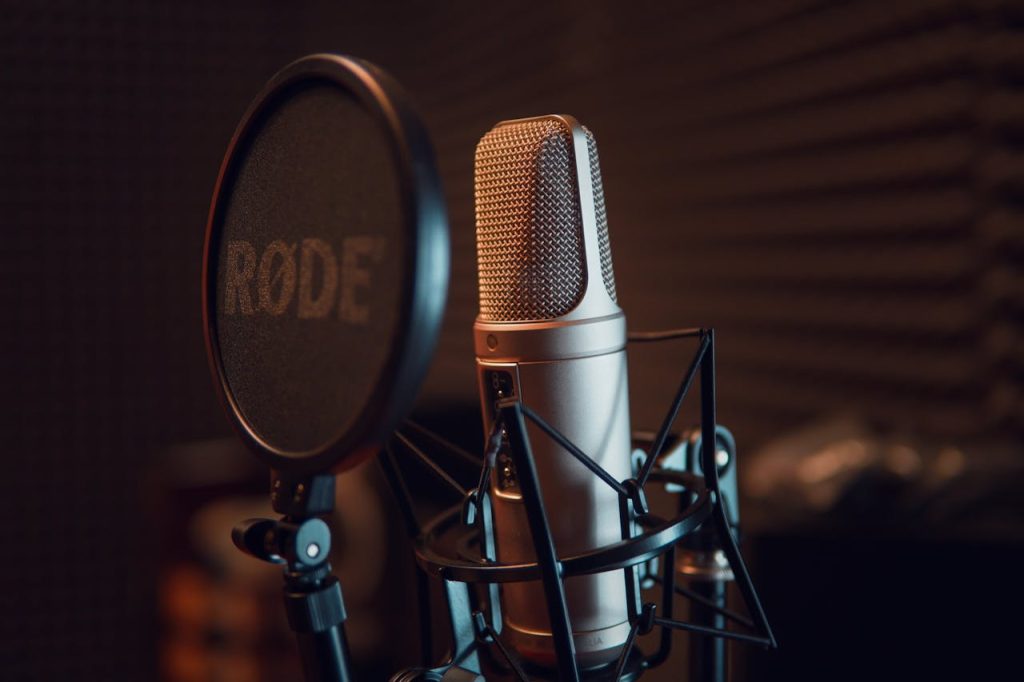 RODE condenser microphone with pop filter in a sound-treated voiceover booth.